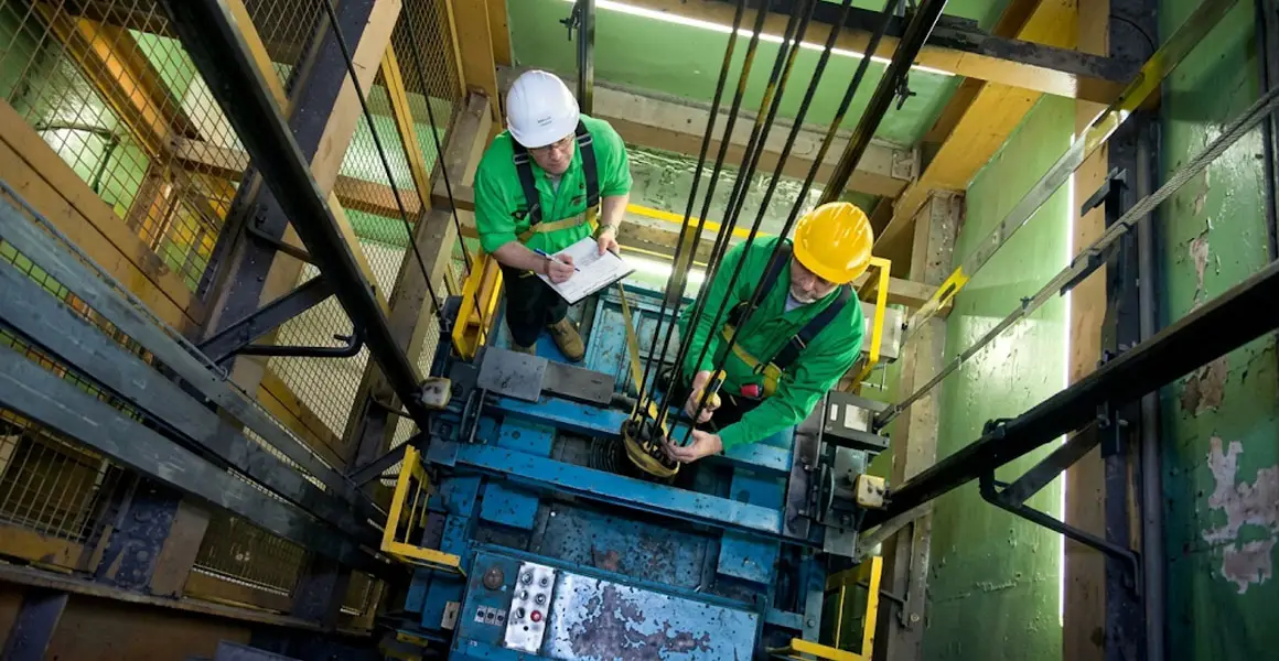Elevator maintenance technicians in safety gear inspecting cables and machinery inside a shaft in Riyadh.
