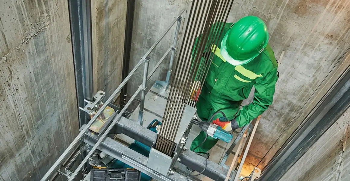 Elevator repair technician in safety gear working on cables and machinery inside a shaft in Riyadh.