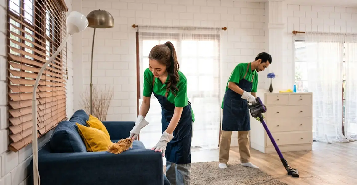 Trained cleaners performing deep home cleaning service in Riyadh – dusting sofa and vacuuming living room floors.