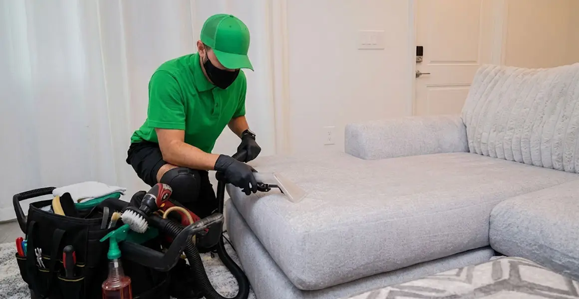 Professional sofa cleaning technician using upholstery extractor on a sectional couch in a Riyadh home.